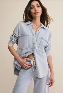  Woman wearing a light blue denim shirt and pants against a beige background