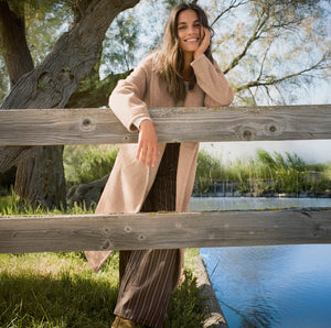  Woman leaning on a wooden fence by a body of water with trees in the background