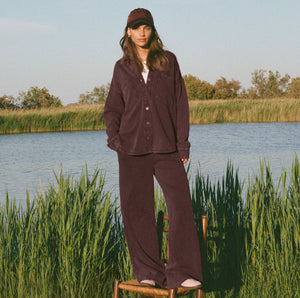  Person wearing a brown outfit standing by a body of water with tall grass.