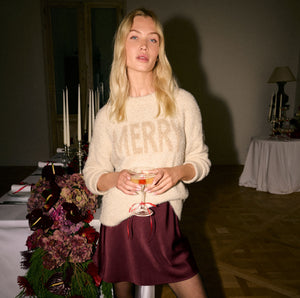  Woman holding a glass in a dimly lit room with tables and flowers.