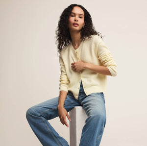  Woman wearing a light yellow cardigan and blue jeans against a plain background