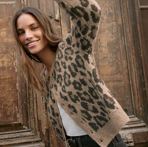  Woman wearing a leopard print cardigan standing against a wooden door.