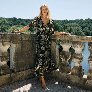  Woman in a floral dress standing on a stone balcony with a scenic background