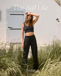  Woman in black athletic wear standing in grass with 'The Soft Life' branding.