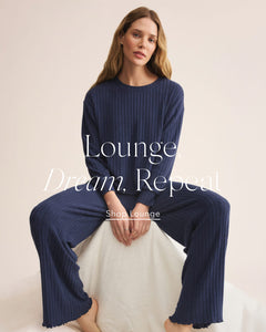  Woman wearing a navy lounge set with text 'Lounge Dream. Repeat' on a beige background