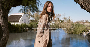  Woman in a beige coat standing by a pond with trees and a house in the background, featuring text about Z Supply's brand story.