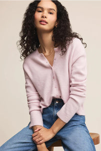  Woman wearing a light pink cardigan over a white shirt with blue jeans on a beige background