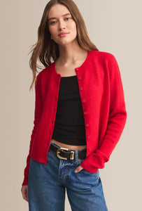  Woman wearing a red cardigan over a black top and blue jeans on a beige background