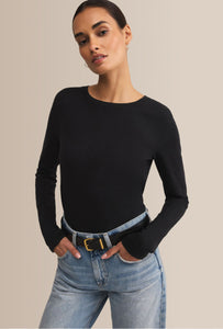 Woman wearing a black long-sleeve top and light blue jeans against a beige background
