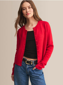  Woman wearing a red cardigan over a black top and blue jeans on a beige background
