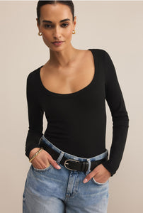  Woman wearing a black long-sleeve top and blue jeans against a beige background