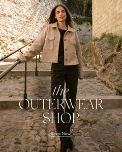  Woman wearing a beige jacket walking outdoors with text 'the OUTERWEAR SHOP' and 'Shop Now'.