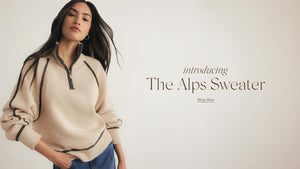  Woman wearing a beige sweater with text 'Introducing The Alps Sweater' on a plain background