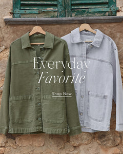  Two jackets, one green and one light blue, hanging on wooden hangers against a rustic stone wall background.