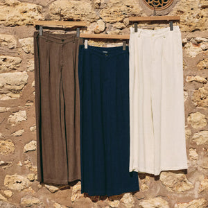 TopsReset French Terry Sweatshirt Three pairs of pants hanging on a wooden rack against a stone wall.