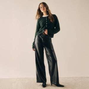  Woman wearing a green cardigan and black pants against a plain background