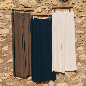  Three pairs of pants hanging on a rack against a stone wall.