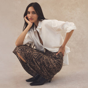  Woman wearing a white blouse and leopard print pants posing against a beige background