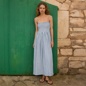  Woman in a blue striped dress standing in front of a green door and stone wall.