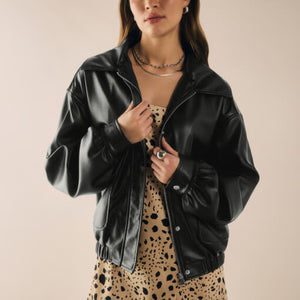  Person wearing a black leather jacket over a patterned dress on a beige background