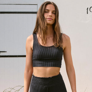  Woman wearing a black ribbed tank top and black pants against a neutral background