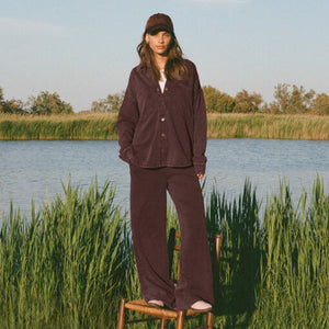 TopsSirena Rib Tank Person wearing a brown outfit standing on a wooden stool by a body of water with reeds.