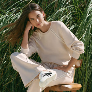  Woman sitting on a wooden chair in a natural setting with greenery.