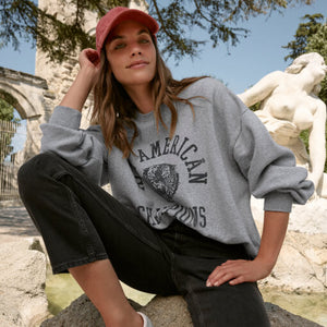 TopsSirena Rib Tank Woman wearing a gray sweatshirt with text and graphics, sitting outdoors near classical statues.