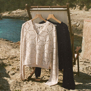  Two sweaters, one white and one black, hanging on a chair by a scenic coastal area.