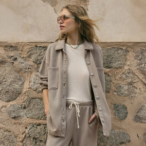  Woman wearing a beige jacket and pants against a stone wall.