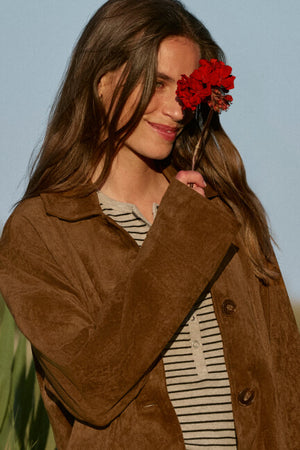 Woman wearing a brown coat with a red flower in her hair against a light blue background