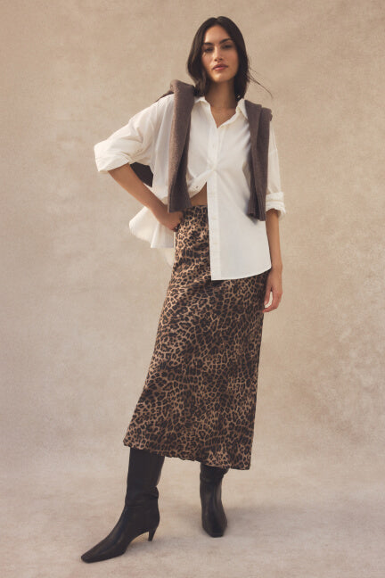 Woman wearing a white shirt, leopard print skirt, and black boots against a beige background