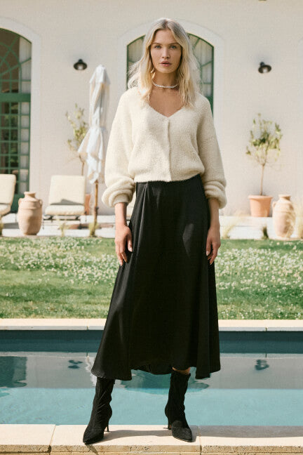Woman standing by a pool wearing a white blouse and black skirt.