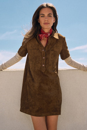 Woman wearing a brown suede dress with a red patterned scarf against a blue sky.