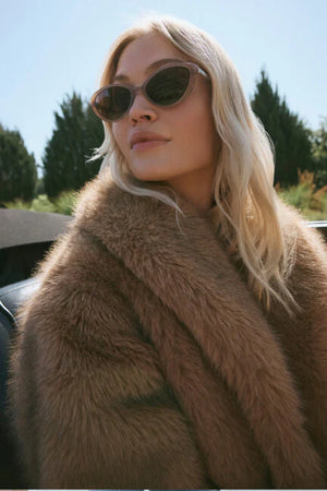 Woman wearing a fur coat and sunglasses with a blurred outdoor background