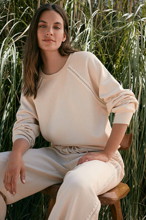 Woman sitting on a wooden stool in a natural setting with tall grasses.