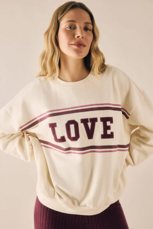 Woman wearing a cream sweatshirt with 'LOVE' printed on it against a beige background