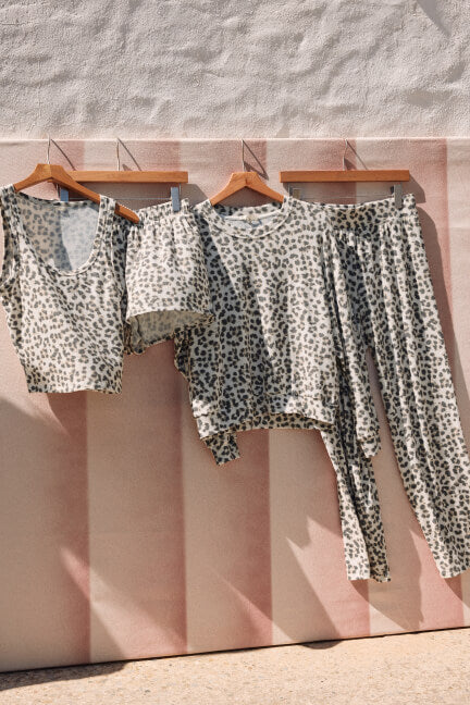 Leopard print pajama set hanging on wooden hangers against a striped wall.